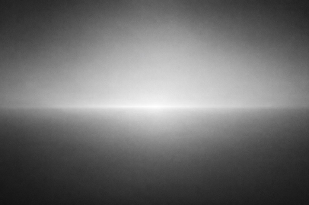 greyscale light emanating from a line of horizon, lighter above and below the line, darker at the edges and corners.